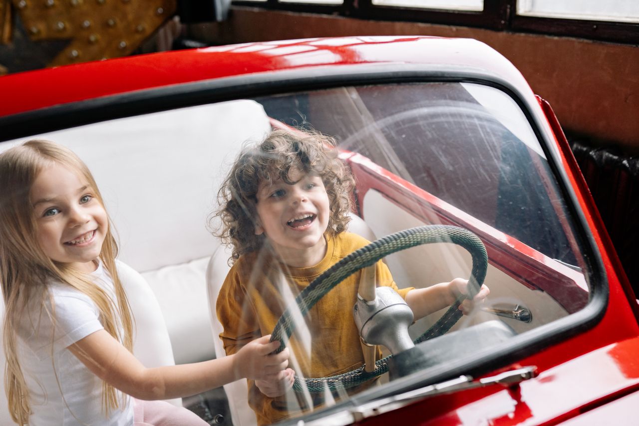 two young children sitting inside car with boy gripping steering wheel